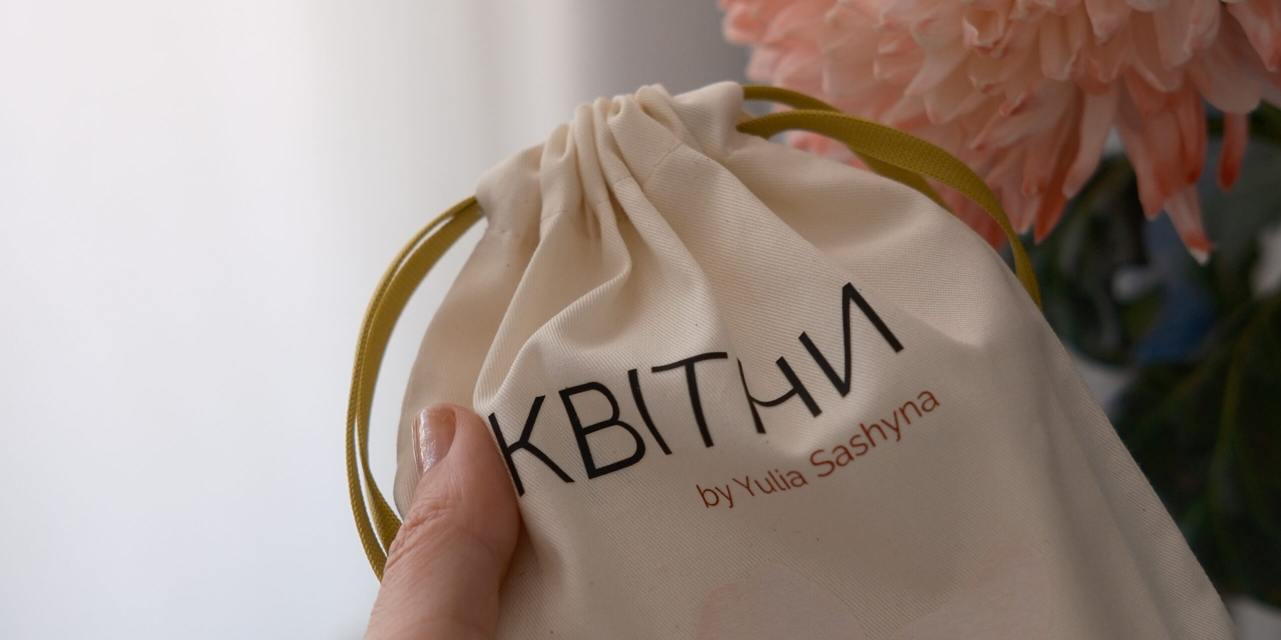 Hand holding the KVITNY deck in its cotton pouch next to a peach dahlia