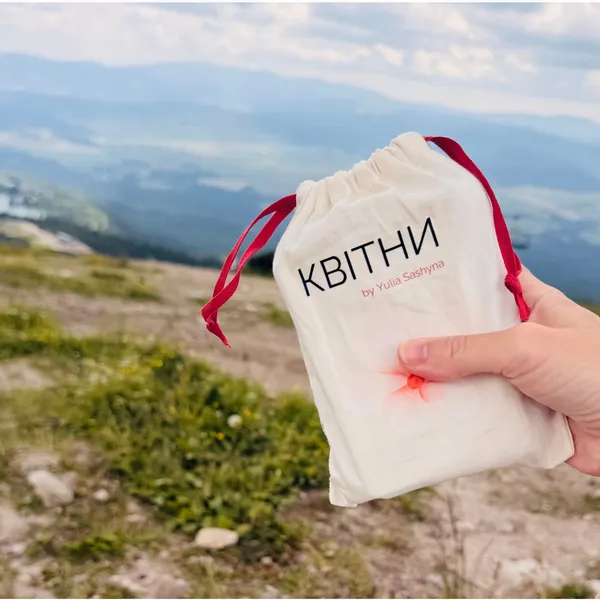 Рука тримає мішечок КВІТНИ на тлі гірської долини